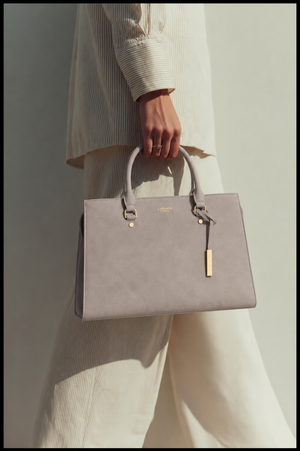 Person holding a gray handbag with a visible brand logo against a neutral background