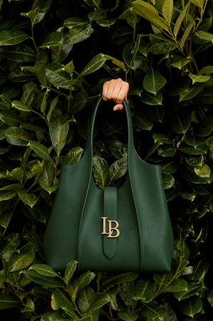 Green handbag with 'LB' logo held by a hand against a leafy green background