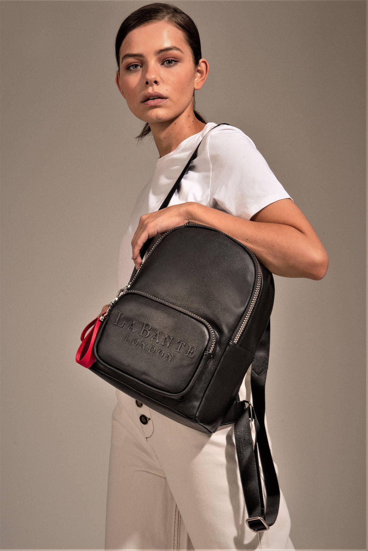 Woman holding a black leather bag with a visible brand logo against a neutral background