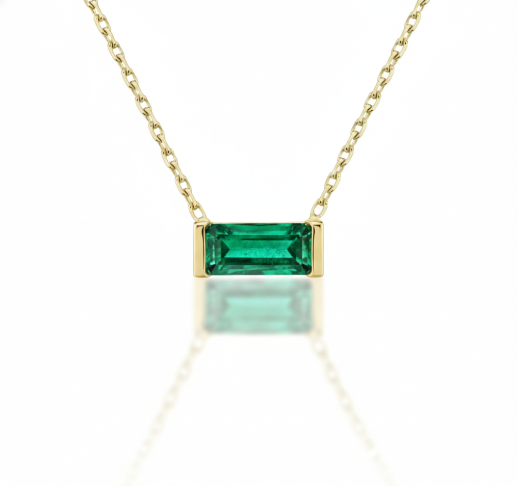 Gold necklace with a green emerald stone on a white background