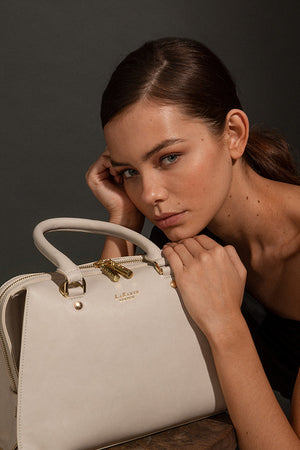 Woman holding a beige handbag with gold accents against a dark background